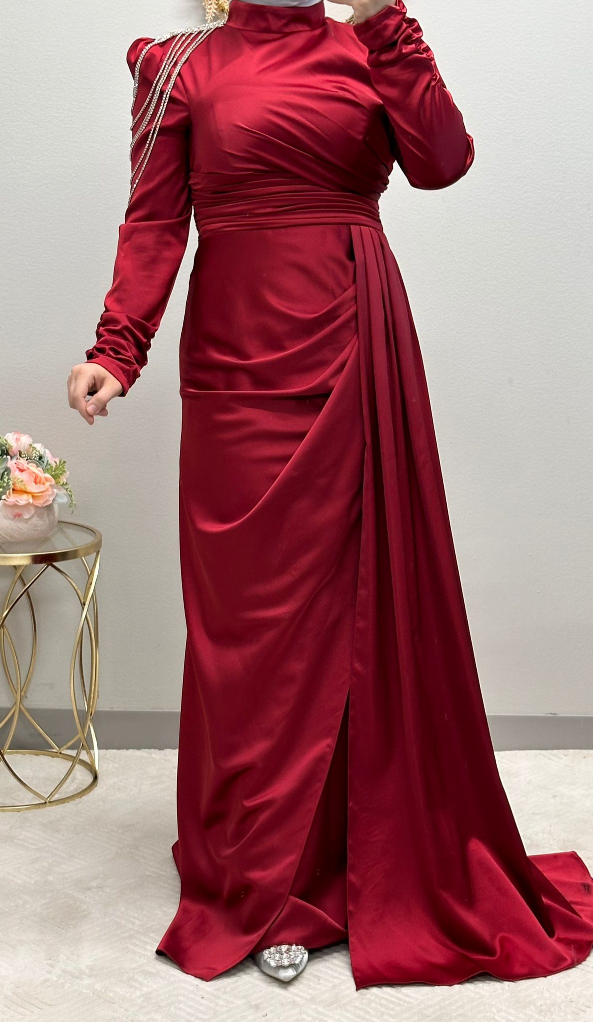 فستان رسمي أحمر مزين بدقة بسلاسل تتدلى على الكتف وطيات متداخلة مصنوعة بدقة. إنه مثال للفخامة، فهو يعرض ثنية جانبية أنيقة، بينما تضفي الأكمام المنتفخة سحرًا ملكيًا.